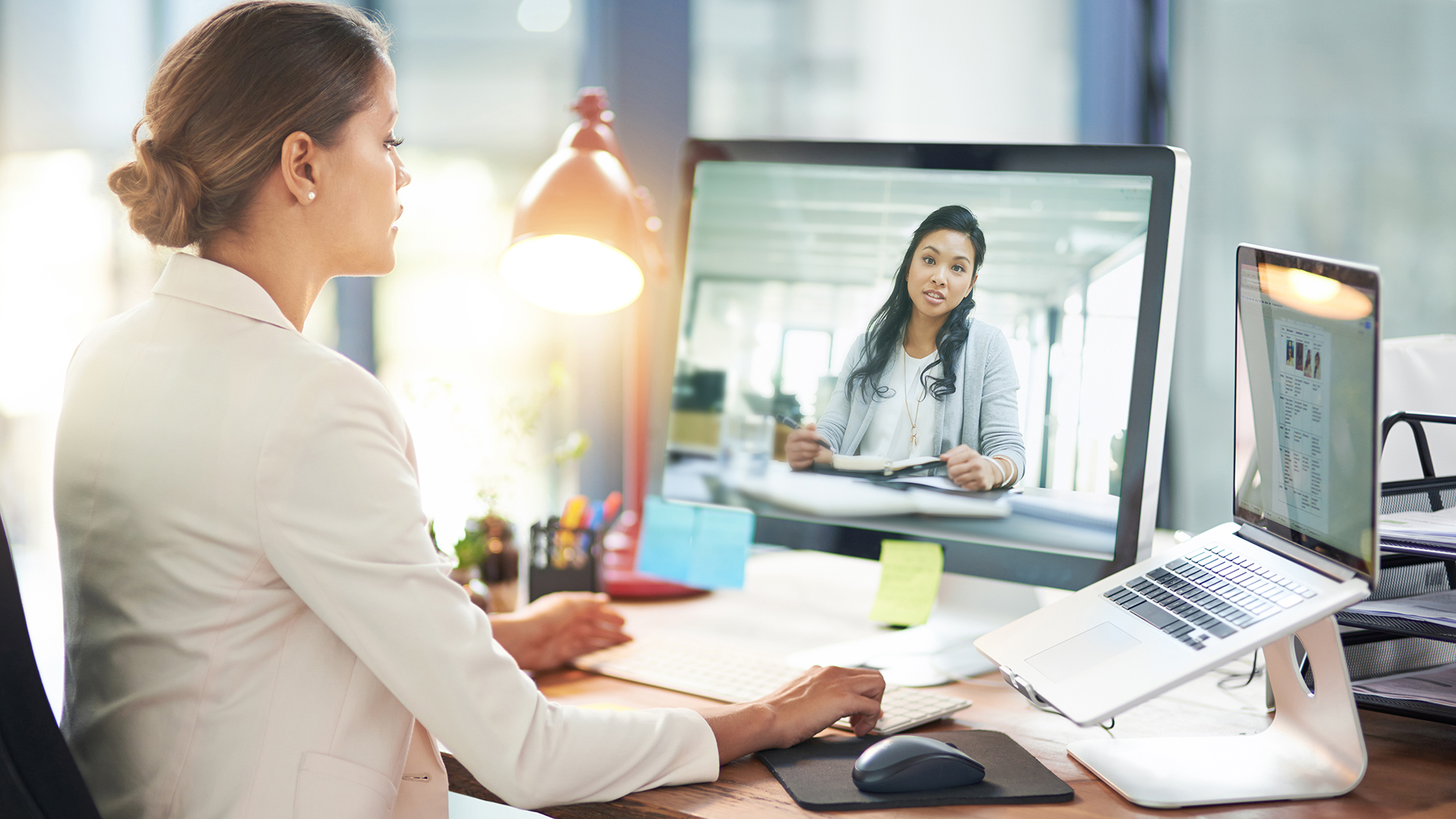 Businesswoman sitting in front of a laptop talking to a remote worker who is visible on the monitor.