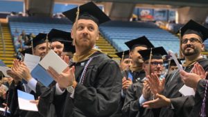 Graduate in cap and gown clapping at UNC Kenan-Flagler ceremony