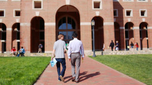 Two male business students walk towards front arches of Kenan-Flagler McColl building