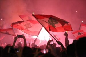 Lebanese flags being waved around in front of red light and smoke