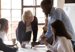 Team of businesspeople sitting and standing around a table looking at reports.