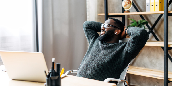 A businessman relaxing at his desk while seated in front of a laptop.