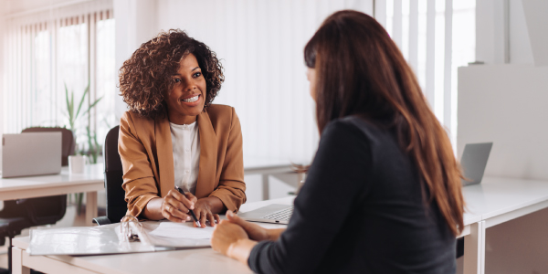 Two businesswomen talking while seated across a desk.