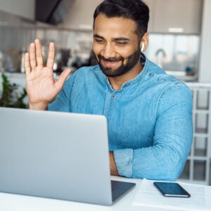 Businessman working from home and sitting in front of a laptop while waving into the webcam.