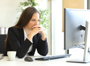 Businesswoman sitting at a desk thinking while looking at a computer monitor.