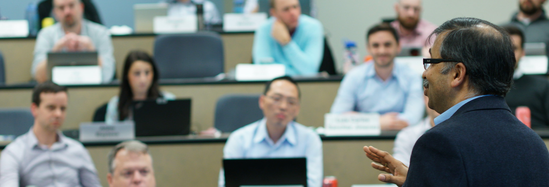A professor stands in front of a room a students. The students look engaged.