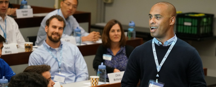 A man stands in front of a room of students. He is giving a presentation.