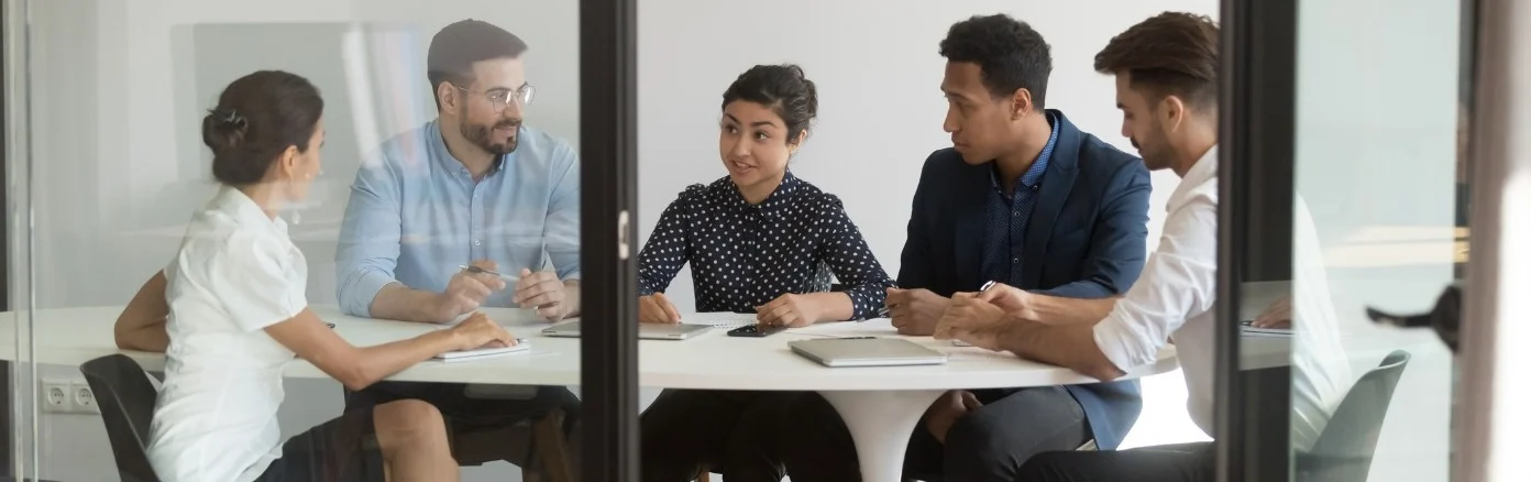 Five businesspeople sit around a table discussing a project.