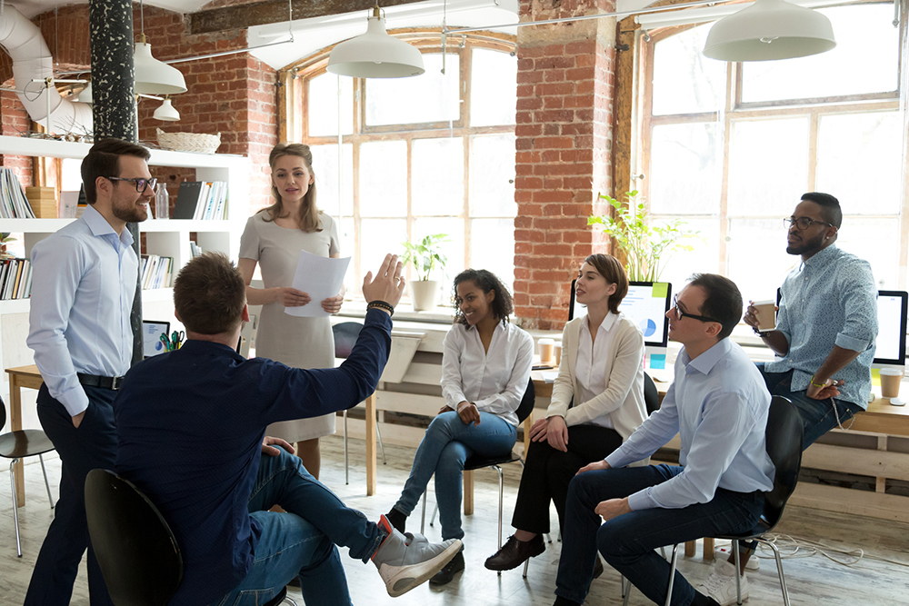 Businessman raising his hand to ask a businesswoman presenter a question during a meeting.