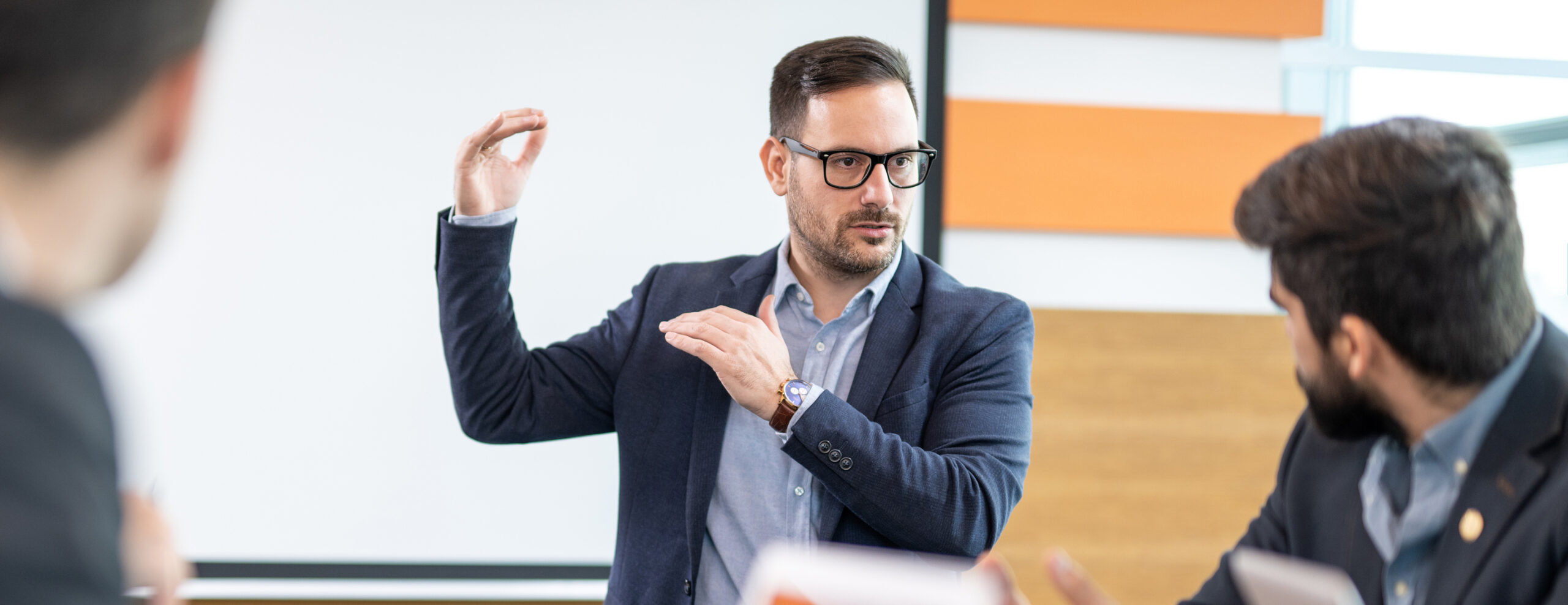 Man gesturing in discussion with others in a professional setting.