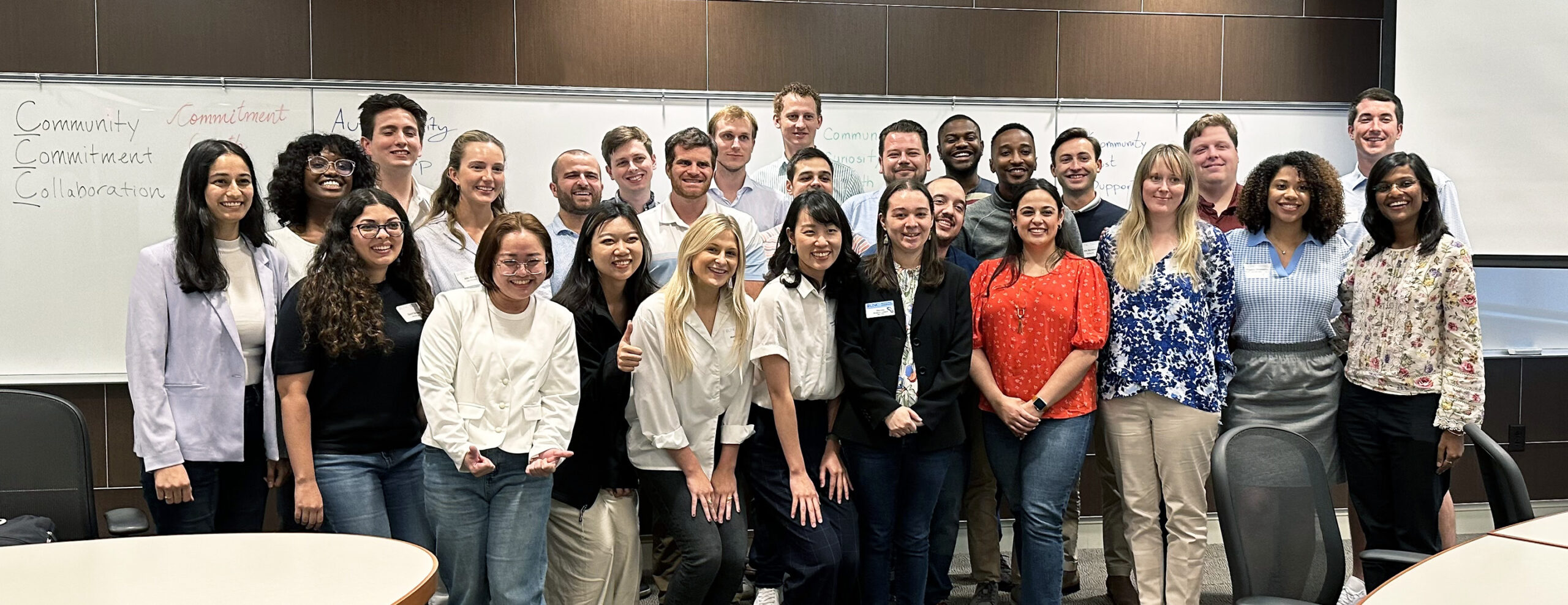 A group of MBA students stands in front of a whiteboard looking at the camera and smiling.