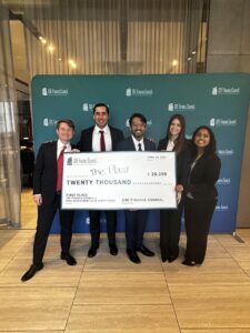 The team smiles while holding a large check in front of a step and repeat for the event.