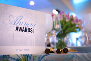 A close-up of the table setting, featuring a sign that reads “Alumni Awards 2025” and a bouquet of pink flowers.