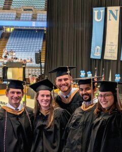 A group of five graduates pose in front of the stage at the graduation ceremony inside the Dean Dome.