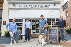 Alumni owners of Carolina Coffee Shop, posing in front of the shop with their dog