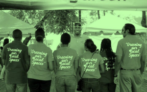 Green tinted image of several people showing the back of their matching shirt which says "Greening out local spaces"