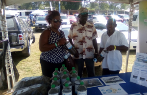 Three people standing at market stand selling fertilizer.