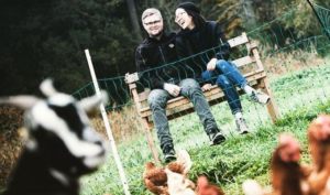 Couple sitting on bench looking over goats and chickens on farm