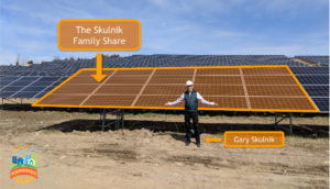 Gary Skulnik standing in front of solar farm, arms outstretched