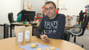 Man sits at table with two paper bags and sliced fruit on a mat.