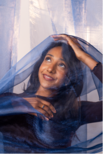 Model posing with jewelry under see-through fabric.