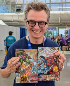 Professor Ric Colacito smiles while holding two signed comic books.