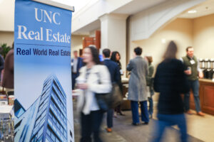 A UNC Real Estate banner with blurred people walking in the background