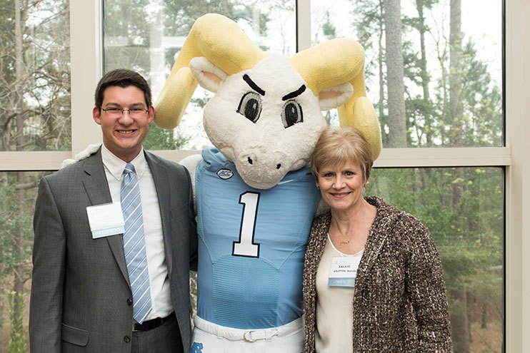 Two people standing with the UNC mascot