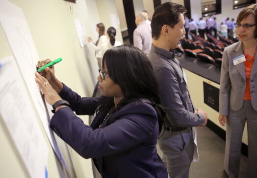 Woman writing on a poster on a wall, with groups discussing behind her and writing on other posters