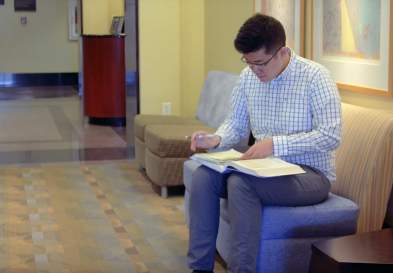 Jack Song sitting in an armless chair, taking notes from a book