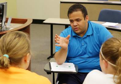 Brandon Ku explaining something and gesturing to three people, in a classroom