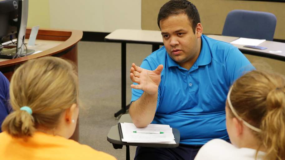 Brandon Ku explaining something and gesturing to three people, in a classroom