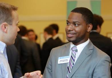 Travis Baten shaking hands with another man, men in suits in the background