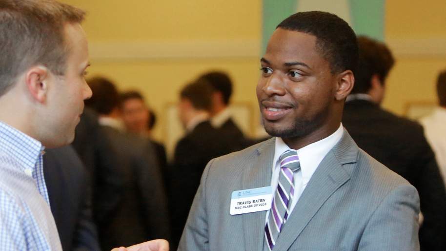 Travis Baten shaking hands with another man, men in suits in the background