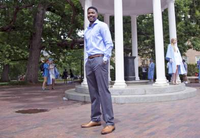 Alexander Jackson standing formally dressed in front of the Old Well and surrounded by people posing for photos in graduation gowns