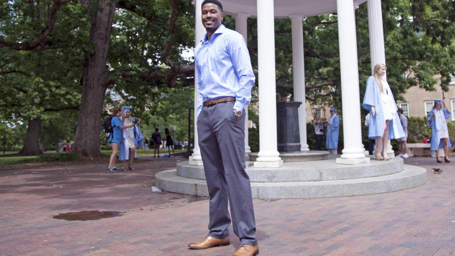Alexander Jackson standing formally dressed in front of the Old Well and surrounded by people posing for photos in graduation gowns