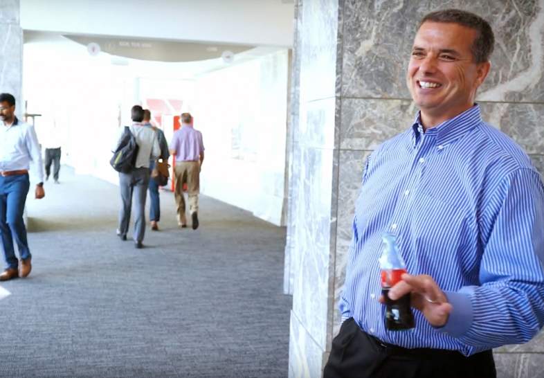 David Byers laughing, holding a bottle of soda, people walking in the background