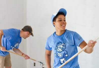 Stephanie and man painting wall in UNC shirt