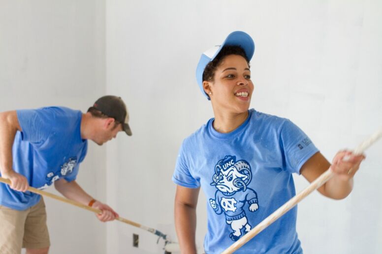 Stephanie and man painting wall in UNC shirt