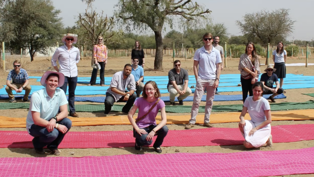 A group of MBA students, some standing and some kneeling, on a multi-colored striped path in an international country looking at the camera smiling.