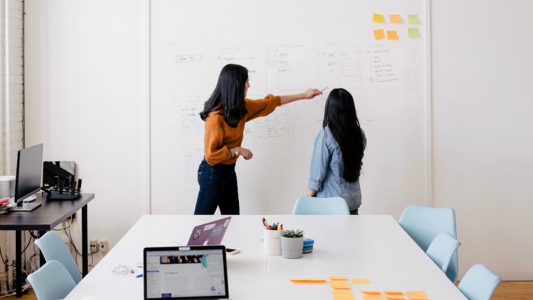 Student and Teacher Talking In Front Of Whiteboard In An Office