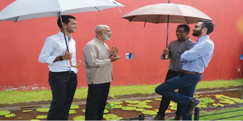 Four men standing outside under umbrellas and talking
