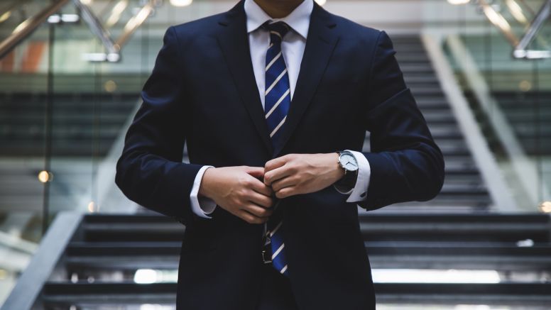 Young man buttoning suit standing in front of stairs