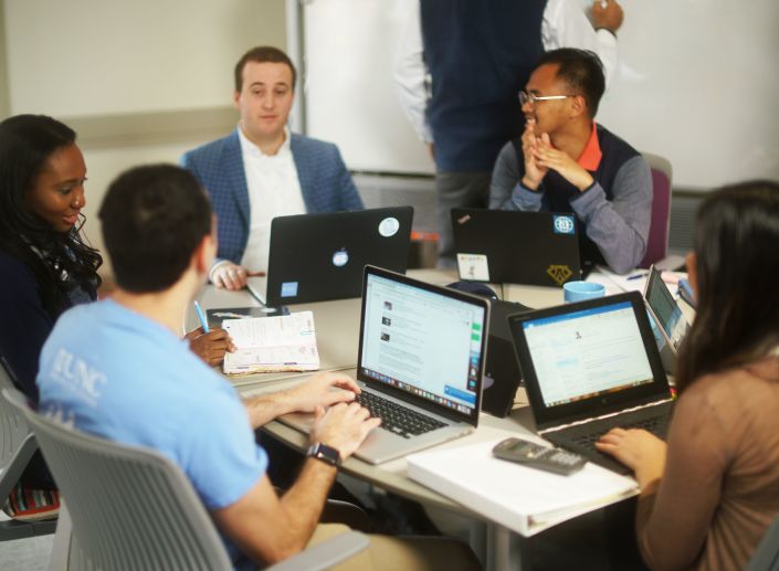 Students sit around a table working together among textbooks and laptops