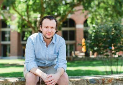 Joe Darcy Smiling Sitting on Stone Wall In Front Of UNC Kenan-Flagler McColl Building