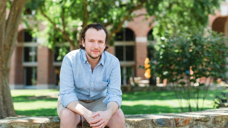 Joe Darcy Smiling Sitting on Stone Wall In Front Of UNC Kenan-Flagler McColl Building