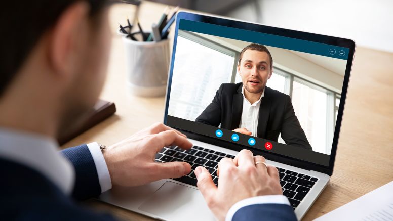 Pc screen view of videoconference over businessman shoulder