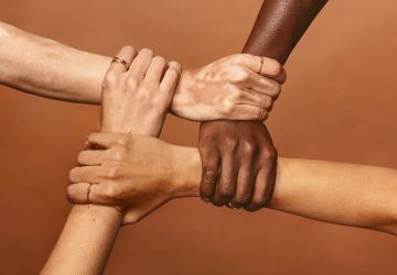 Four diverse hands holding each others wrists in a circle.