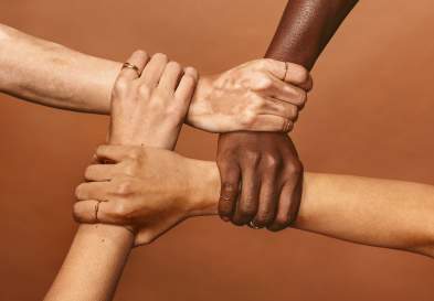 Four diverse hands holding each others wrists in a circle.