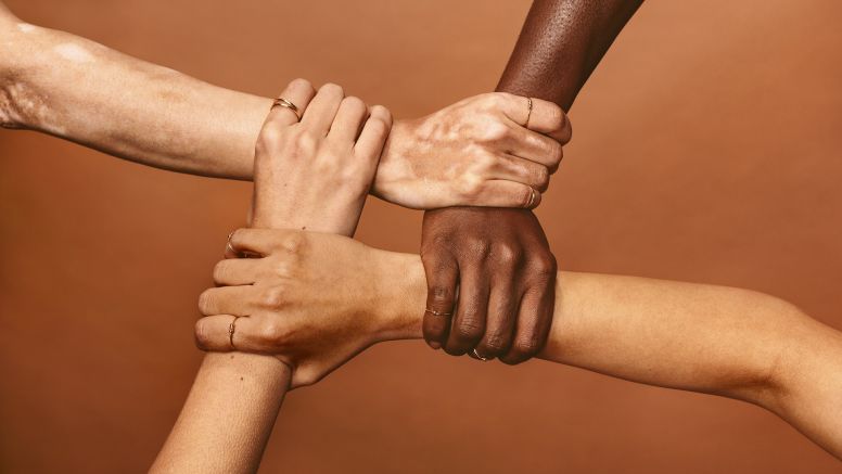 Four diverse hands holding each others wrists in a circle.